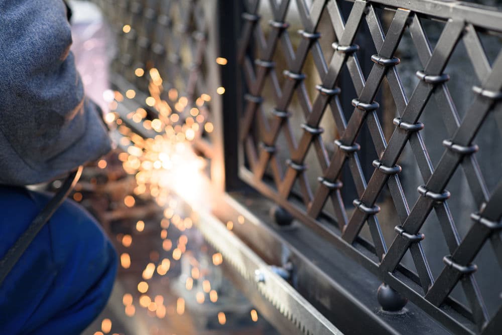 Welding sparks flying while crafting a decorative metal fence with a diamond pattern.